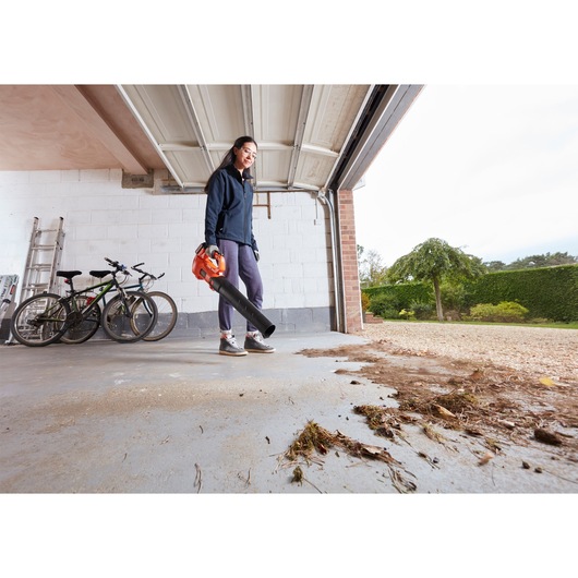 BLACKDECKER BCBL200L cordless leaf blower used to clear debris from garage floor, outdoor angle.