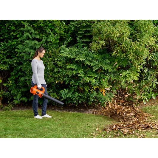 Person using BLACKDECKER BCBL200L cordless leaf blower on garden leaves, orange and black in color.