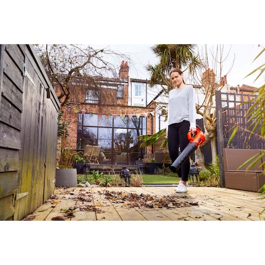 BLACKDECKER BCBL200L leaf blower held by person clearing leaves on wooden patio in garden.