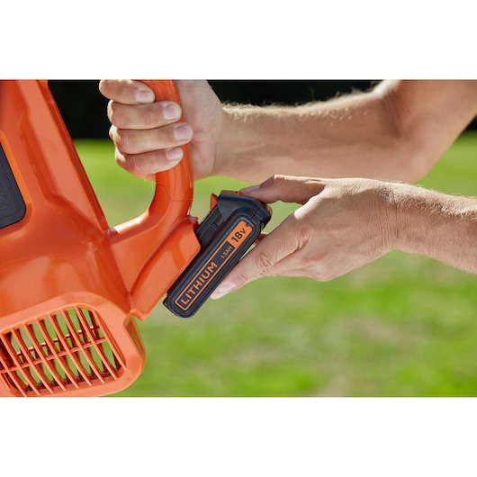 Photo of a BLACKDECKER BCBL200L orange leaf blower with close-up of 18V lithium battery being inserted outdoors.