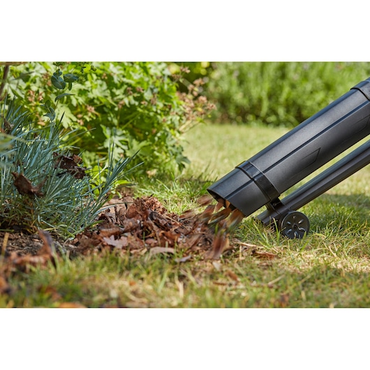 BLACKDECKER BCBLV3620L1 leaf blower nozzle dispersing leaves onto grass, close-up outdoor view.
