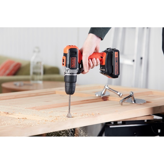 BLACKDECKER BCD003C1 cordless drill in use on wood, close-up view showing orange and black design.
