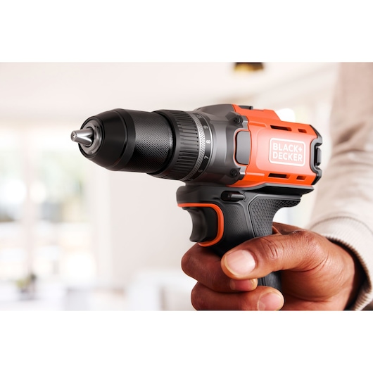 Hand holding a BLACK+DECKER cordless drill in a bright indoor setting.