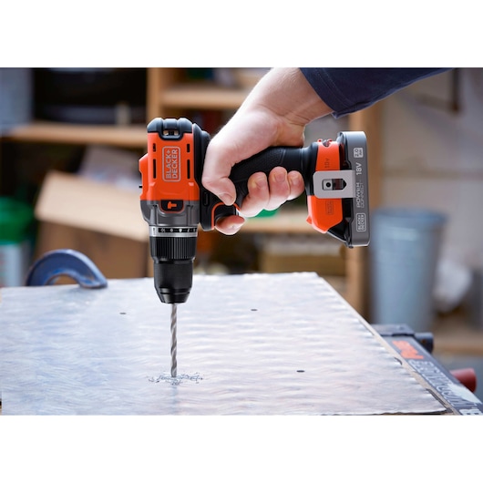BLACK+DECKER cordless drill in use, drilling through a metal surface in a workshop.