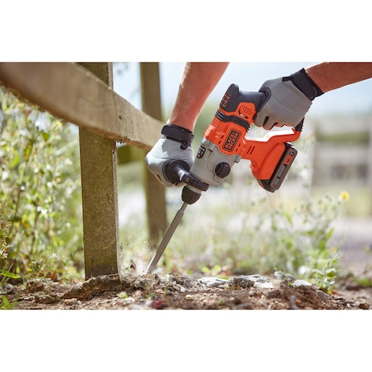 Photo of BLACK+DECKER BCD900D1K cordless rotary hammer in use outdoors with a chisel attachment.
