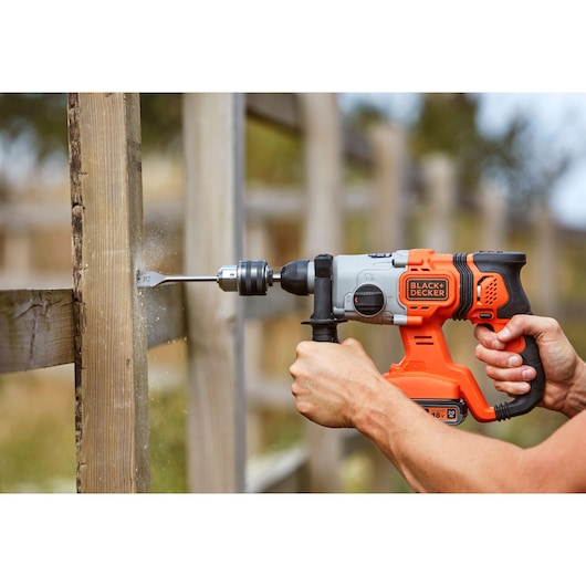 BLACK+DECKER BCD900D1K cordless hammer drill in use on outdoor wooden post.