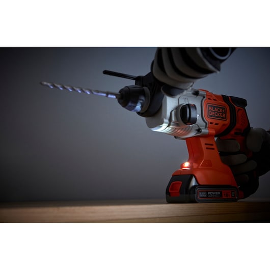 BLACKDECKER BCD900D1K cordless hammer drill in use, side view, orange and black with LED light on.