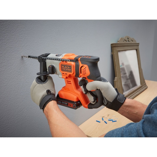 BLACK+DECKER BCD900D1K cordless hammer drill in use drilling into a wall, close-up side angle.
