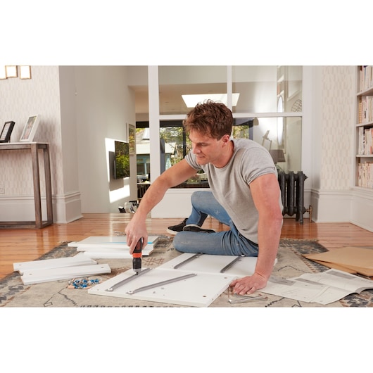 Photo of person assembling furniture with BLACKDECKER cordless screwdriver BCF601C indoors on rug.