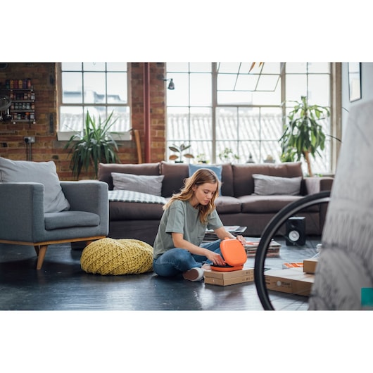 BLACKDECKER BCF611CK tool kit in orange case, person sitting on floor in modern living room setting.