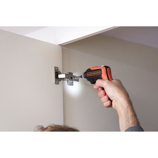 Photo of BLACK+DECKER BCF611CK cordless screwdriver in use on cabinet hinge with LED light.