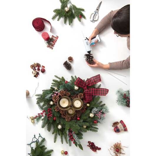 Photo of BLACKDECKER BCGL115 hot glue gun used in holiday wreath crafting with pinecones, candles, and festive decorations.