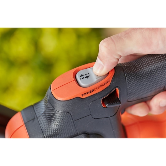 Close-up of BLACK+DECKER BCHTS36B hedge trimmer handle with hand pressing PowerCommand button.