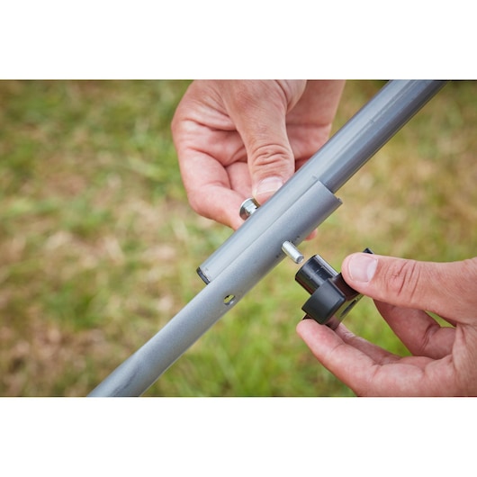 Close-up photo of hands assembling BLACK+DECKER BCMW33182L2 lawn mower handle with a bolt and knob outdoors.