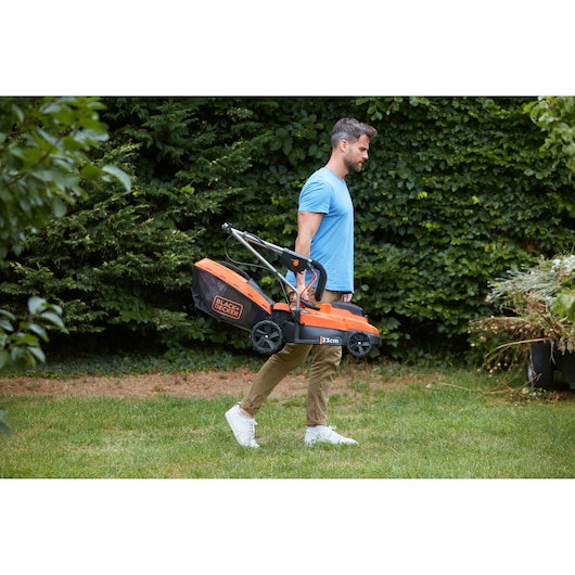 Photo of BLACKDECKER BCMW3318N lawn mower with orange and black design carried outdoors by a person.