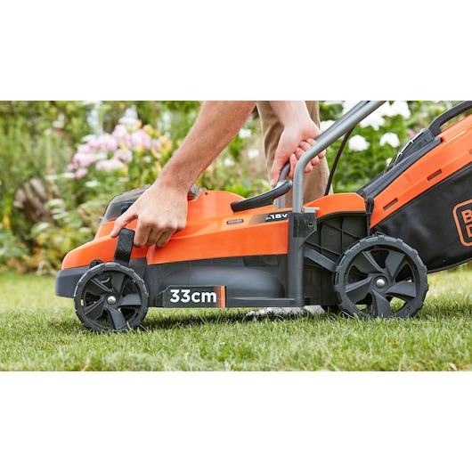 Photo of BLACK+DECKER BCMW3318N lawn mower, orange and black, side view, user adjusting handle, 33cm cutting width.