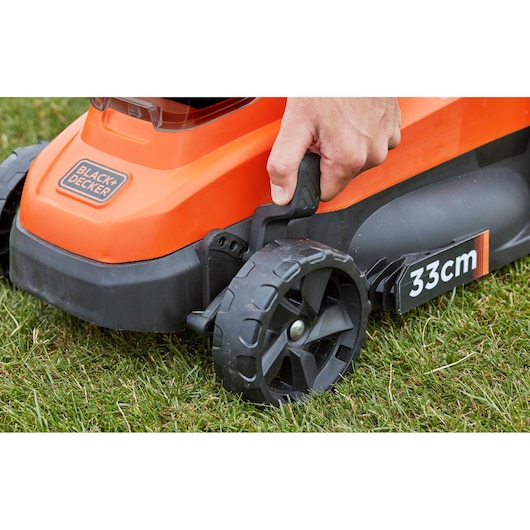 BLACK+DECKER BCMW3318N lawn mower side view with a hand adjusting wheel height on grass, 33cm cutting width visible.