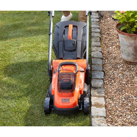 BLACKDECKER BCMW3336N lawn mower front view on grass next to stone border and flower pot.