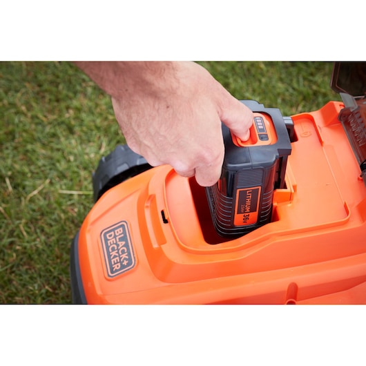 Photo of BLACK+DECKER BCMW3336N lawn mower battery compartment with hand inserting 36V lithium battery.