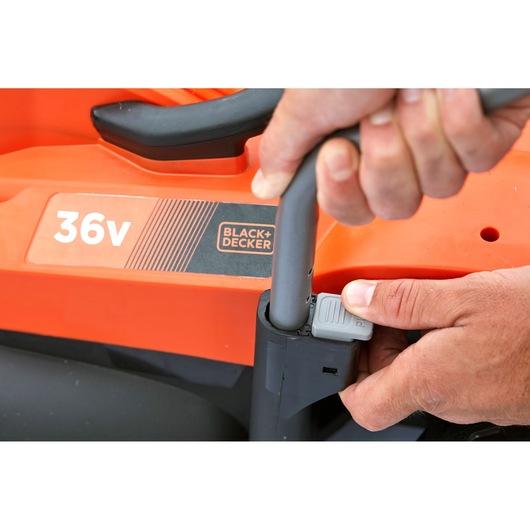 Close-up of hands adjusting BLACK+DECKER BCMW3336N 36V lawn mower handle with visible orange body.