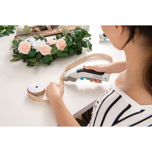 BLACKDECKER BCSC115 handheld cutting tool used to cut ribbon for floral crafts on a white table.
