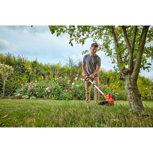 Photo of BLACKDECKER BCSTA536B grass trimmer used in a garden with flowers and trees.