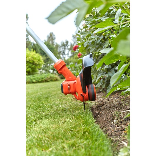 BLACKDECKER BCSTA536B grass trimmer close-up cutting lawn edge near garden plants outdoors.