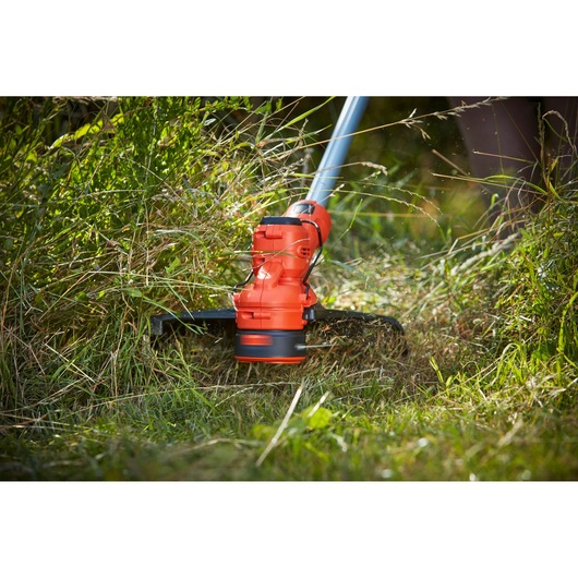 BLACKDECKER BCSTA536B grass trimmer in use, red and black head cutting tall grass.