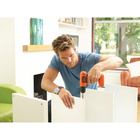 BLACKDECKER BDCD8 cordless drill used for assembling white furniture indoors.