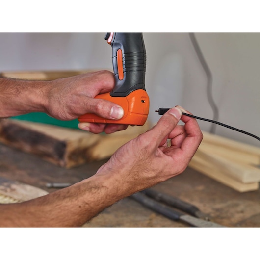 Photo of BLACKDECKER BDCD8 cordless drill being charged with a cable in a workshop setting.