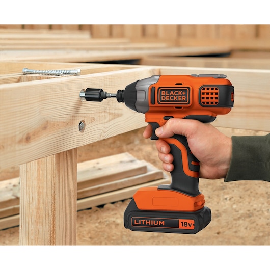 BLACK+DECKER BDCIM18C1 18V cordless impact driver being used to drive a screw into wood, close-up.
