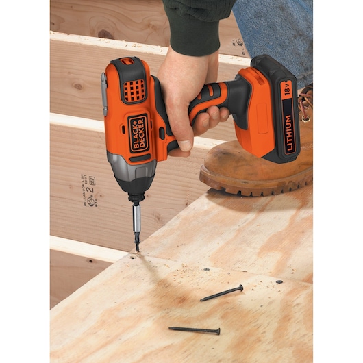 BLACK+DECKER BDCIM18C1 orange cordless impact driver in use on wood construction, close-up angle.