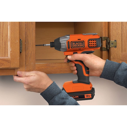 BLACK+DECKER BDCIM18C1 18V cordless impact driver used to install a screw in wooden cabinet door.