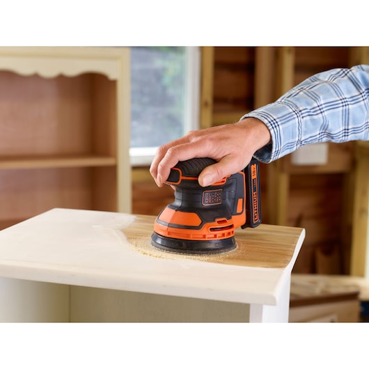 BLACKDECKER BDCROS18 cordless random orbital sander sanding wood surface in workshop.
