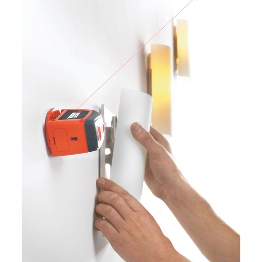 BLACKDECKER BDL120 laser level tool mounted on a wall projecting a red line, hands aligning a fixture.