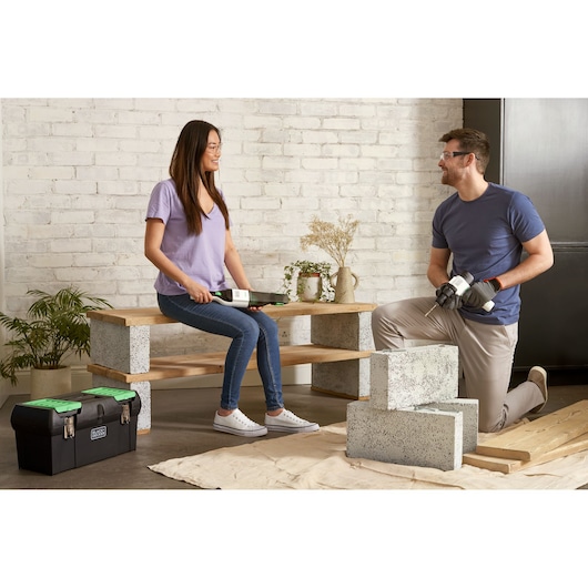 BLACKDECKER BDST60120 black toolbox with green latches on floor, indoor setting with cinder blocks and wood.