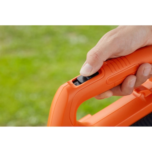 Close-up photo of a hand pressing the BLACK+DECKER BEBL185 orange blower handle trigger outdoors.
