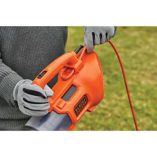 Photo of BLACK+DECKER BEBL185 orange corded leaf blower held by person wearing gray gloves outdoors.