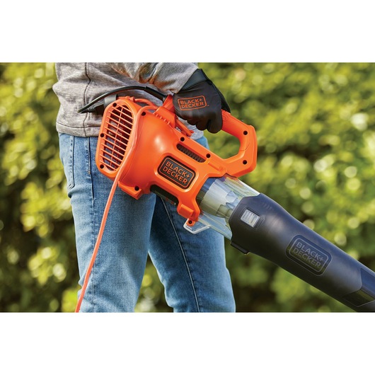 Photo of BLACK+DECKER BEBL185 orange and black corded electric leaf blower held by person wearing gloves outdoors.