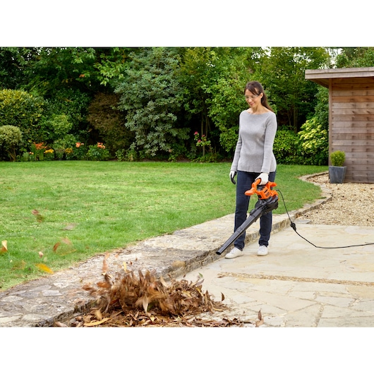 BLACKDECKER BEBLV260 corded leaf blower in use outdoors clearing leaves from stone patio, side photography.