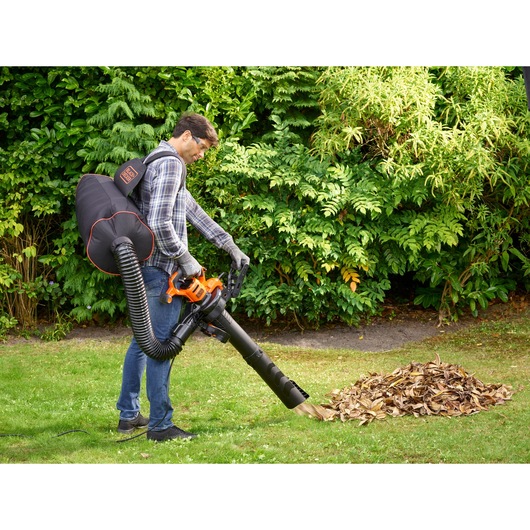 BLACKDECKER BEBLV301 leaf blower with collection bag in outdoor garden setting.