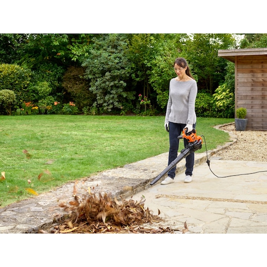Photo of BLACKDECKER BEBLV301 leaf blower in use on patio with leaves blowing, garden in background.