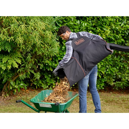 BLACKDECKER BEBLV301 garden vacuum bag pouring mulch into green wheelbarrow outdoors.
