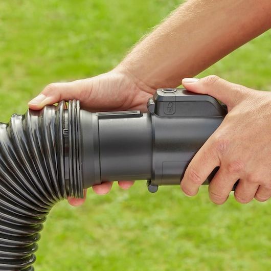 Photo of BLACK+DECKER BEBLV301 garden vacuum hose connection detail, hands attaching black flexible hose outdoors.