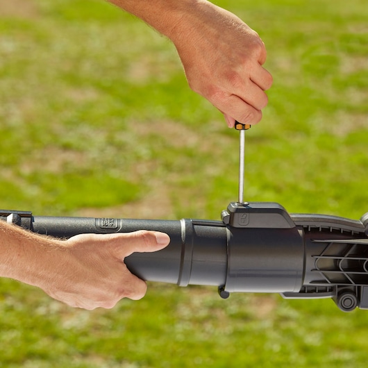 Close-up photo of hands assembling BLACKDECKER BEBLV301 leaf blower tube with a screwdriver outdoors.