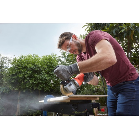 BLACKDECKER BEG010A5 circular saw used outdoors for cutting wood, person wearing gloves and safety glasses.