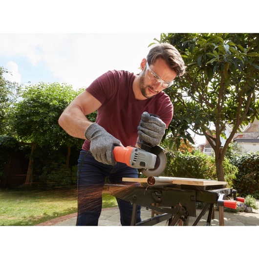 Photo of BLACKDECKER BEG010A5 angle grinder in use outdoors, cutting metal with sparks and gloves visible.