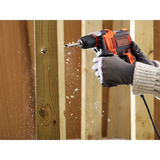 BLACK+DECKER BEH710K corded drill in use drilling wood, close-up of hand wearing gloves.