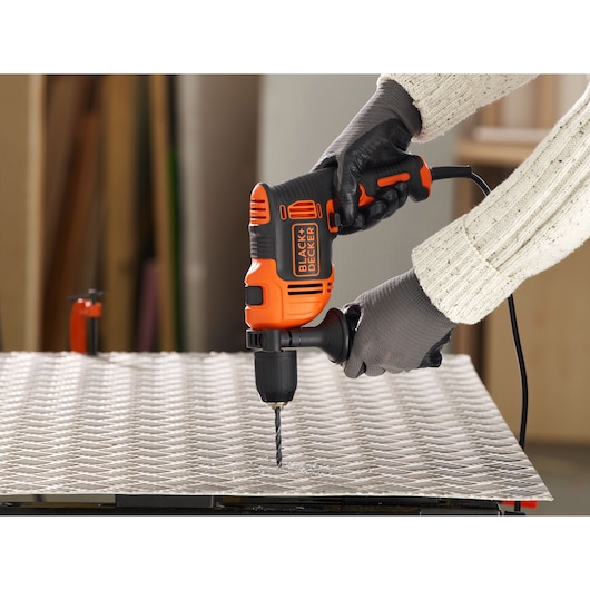 BLACK+DECKER BEH710K corded drill in use on metal sheet, orange-black, held with gloves.