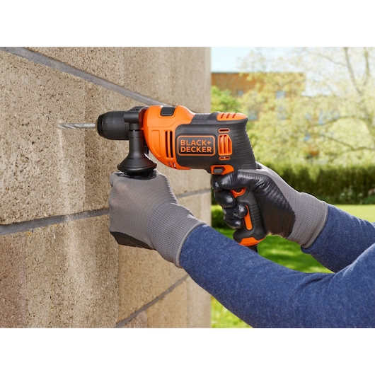 BLACKDECKER BEH710K orange cordless drill in use on concrete wall outdoors, close-up view.